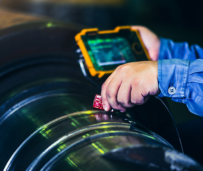 检查和检测 - 一个人正手持设备检查一个大型圆柱形金属物体，可能是出于质量控制或测量目的。